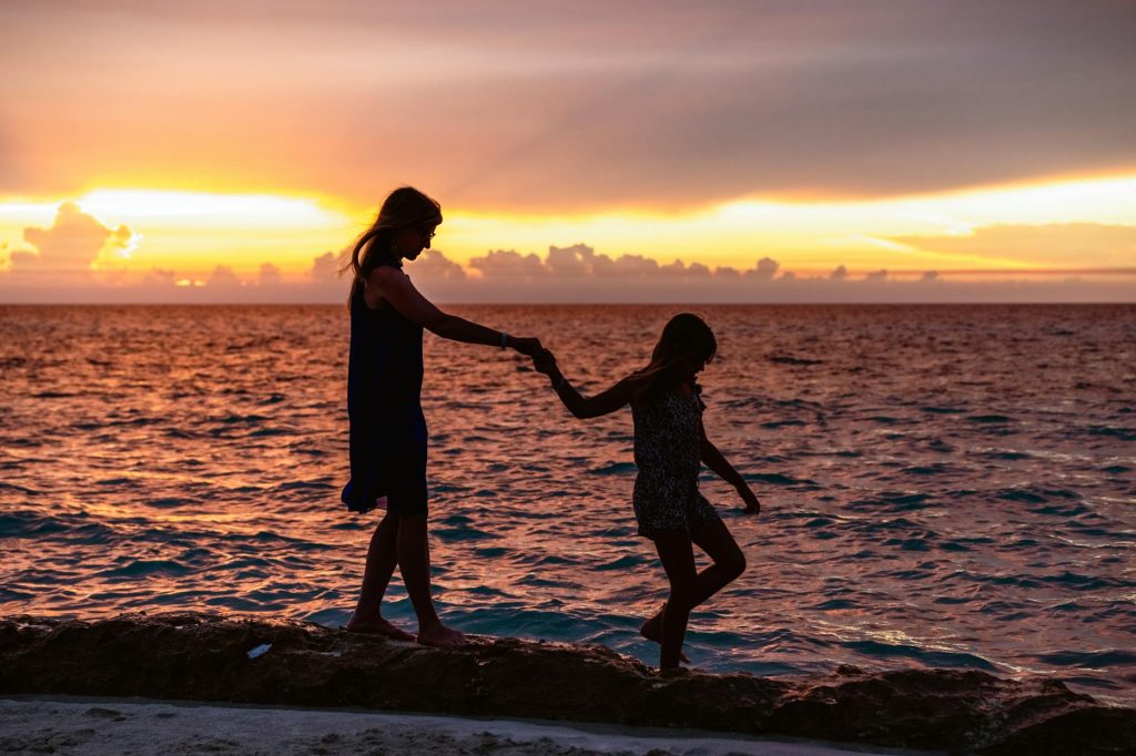 Une mère et sa fille marchant ensemble sur une plage tropicale au coucher du soleil
